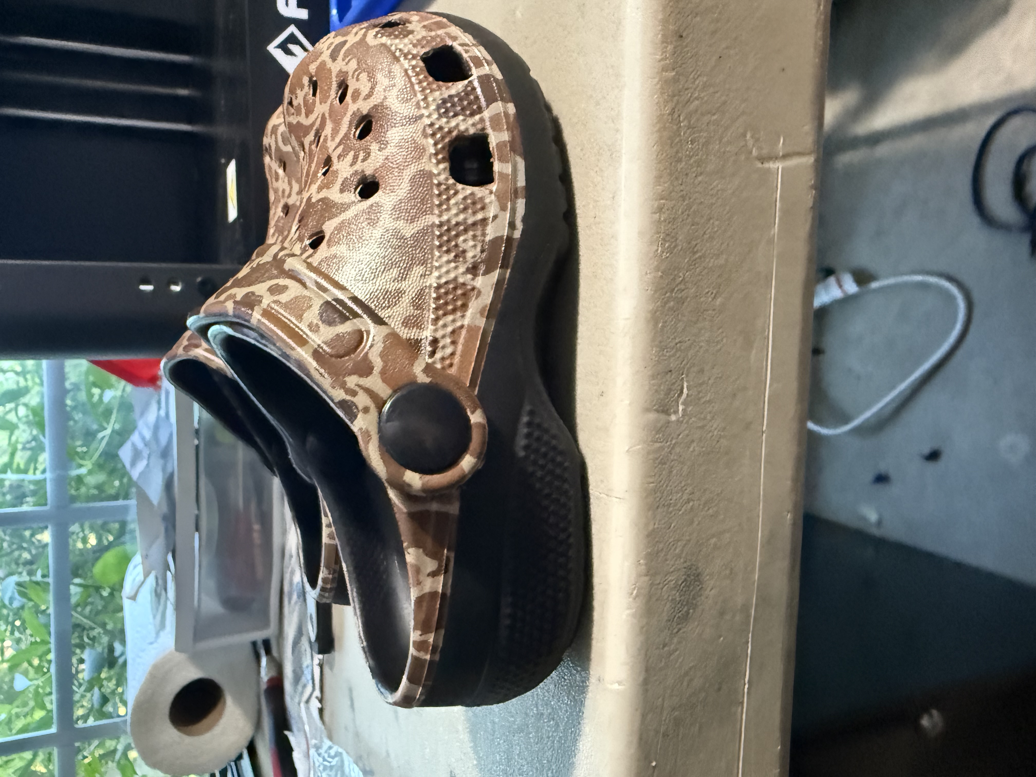 Angled side view of two customized Crocs on a worktable, showing the patterned uppers, straps, and black soles.