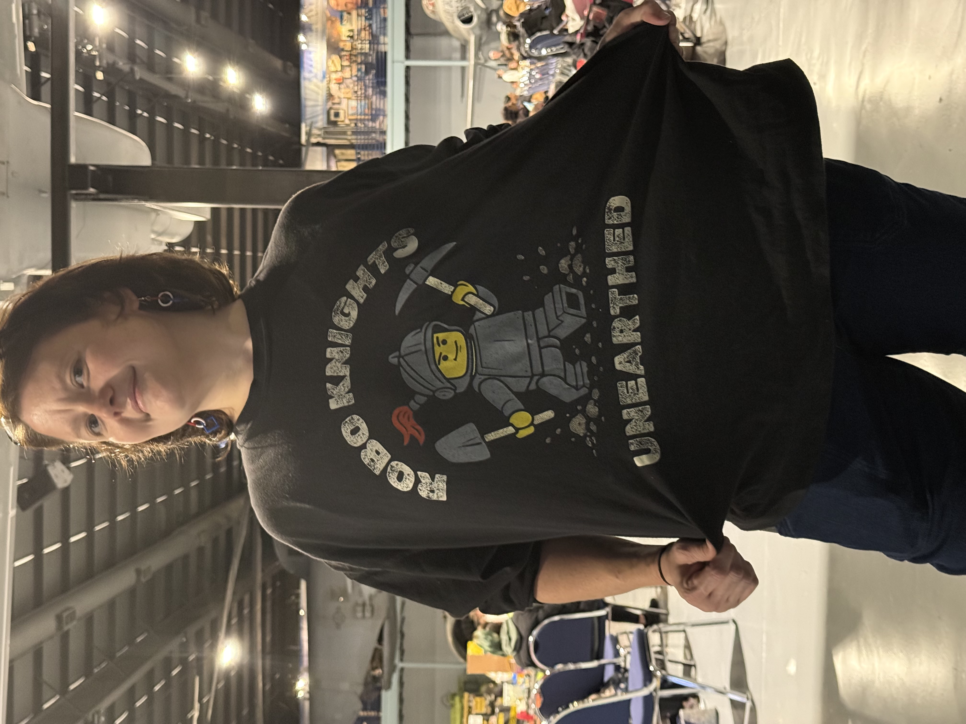 Front of a dark Robo Knights shirt held out to show a knight graphic and the word UNEARTHED.